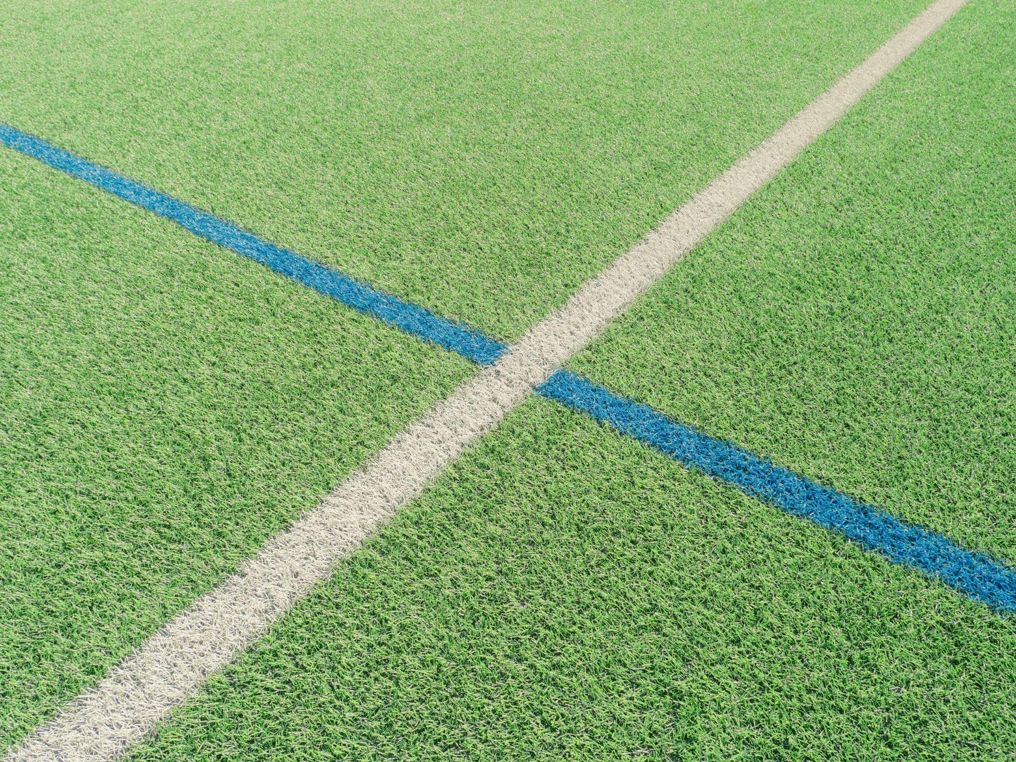 Green sports field with intersecting white and blue lines in bright sunlight