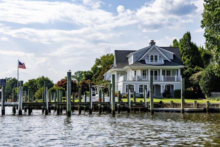 Large white house with balcony by waterfront dock under partly cloudy sky