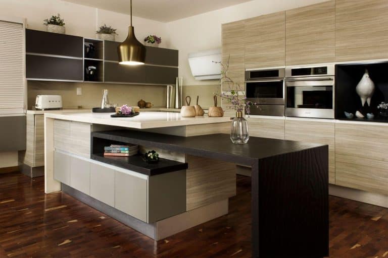 Modern kitchen with wooden cabinetry, pendant light, and decorative plants on polished countertops
