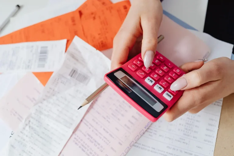 Hands holding red calculator with receipts and pencil on cluttered desk