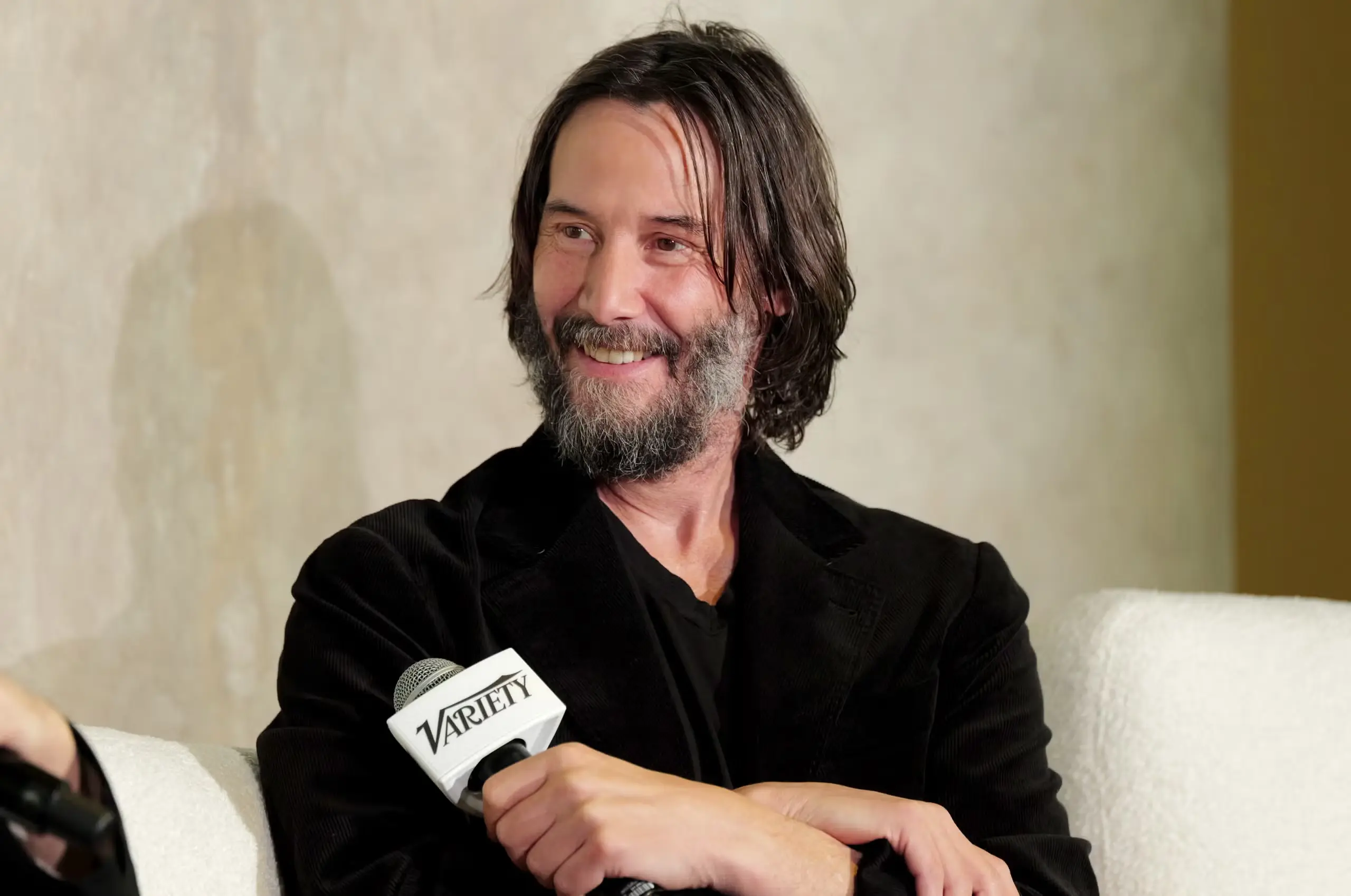 Keanu Reeves smiling while speaking into a Variety microphone at an interview panel.