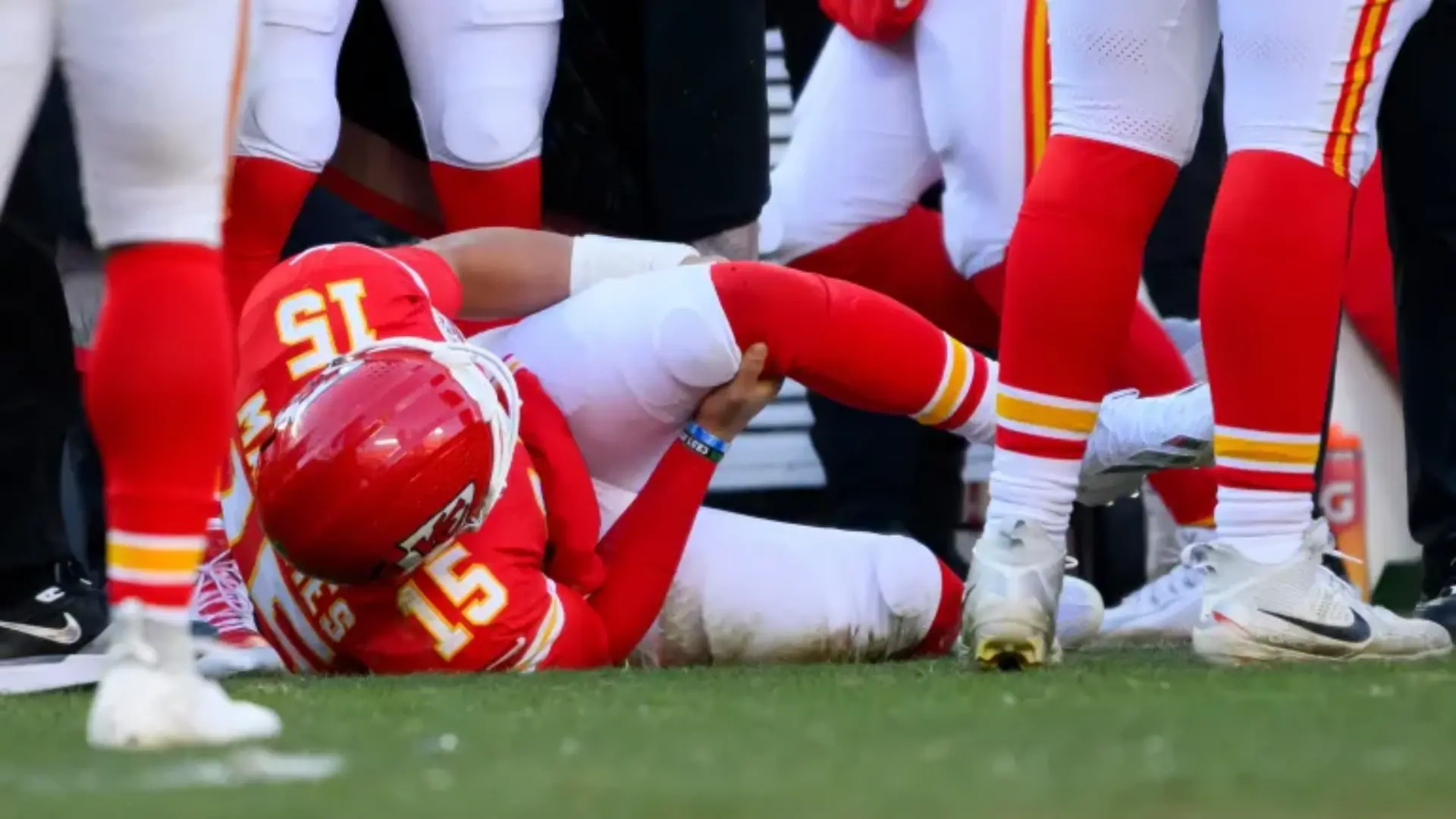 Patrick Mahomes wearing No. 15 lies on the field holding his leg as teammates gather around.