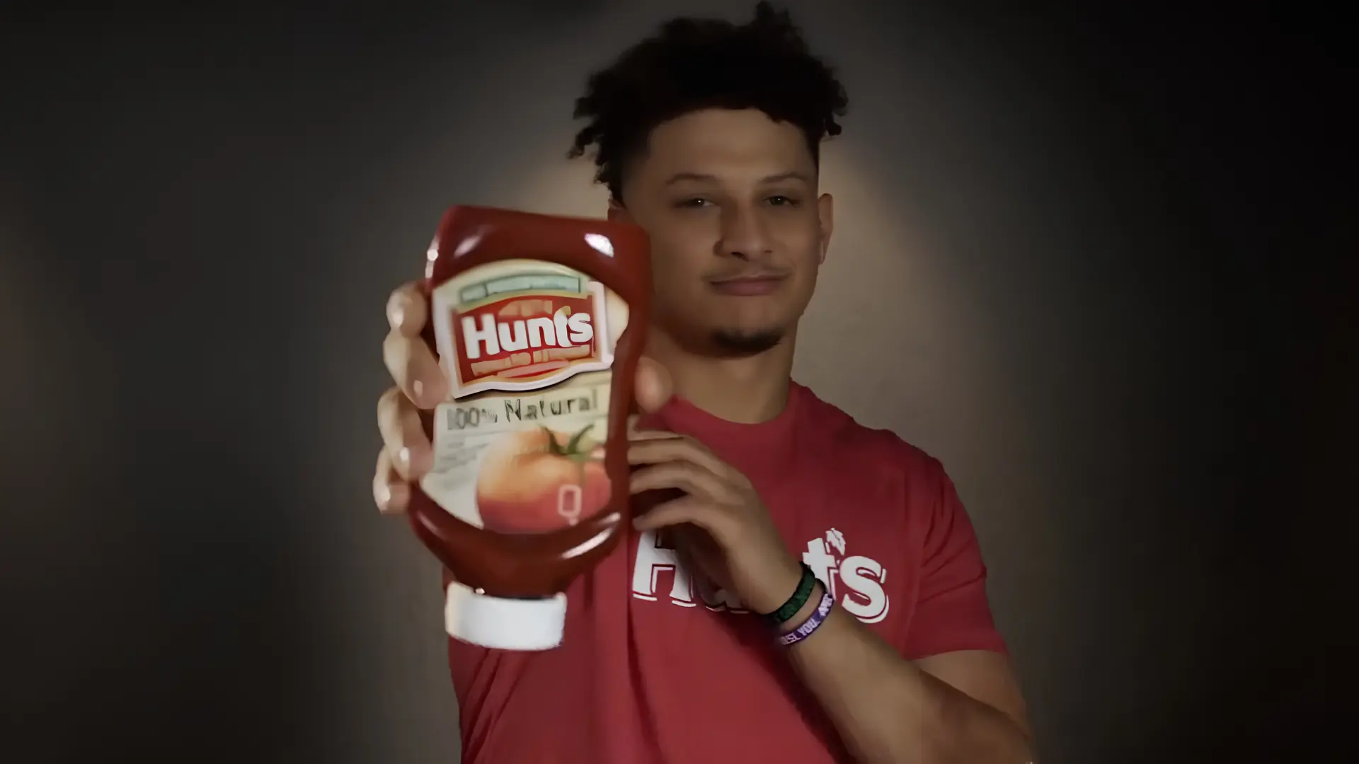 Patrick Mahomes red shirt holding a bottle of Hunt&rsquo;s ketchup toward the camera.