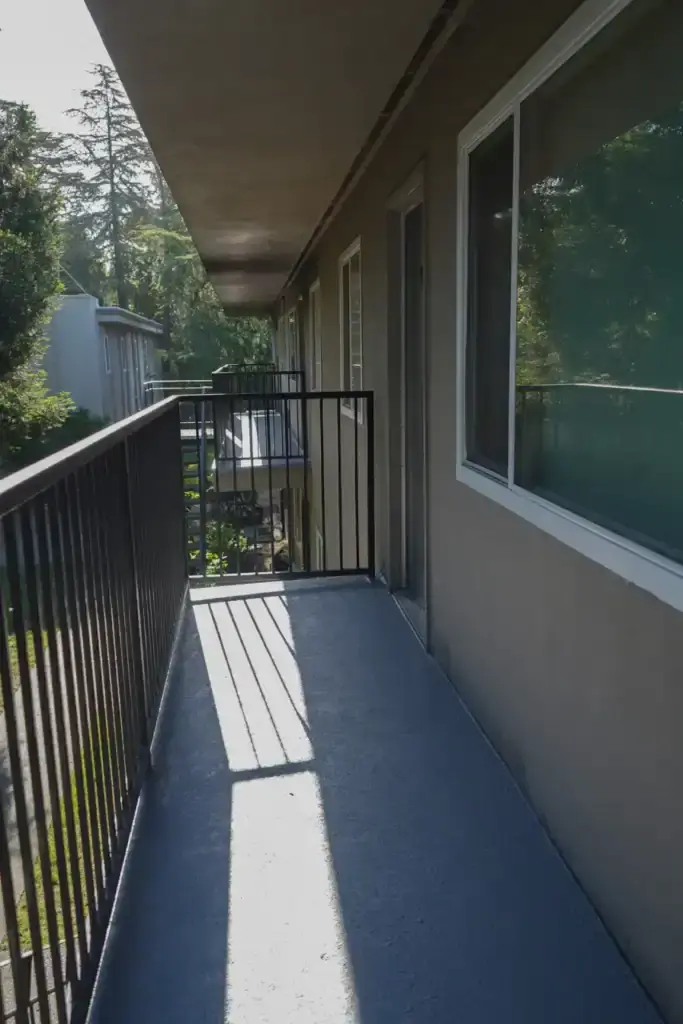 Apartment balcony corridor with metal railing and sunlight casting shadows