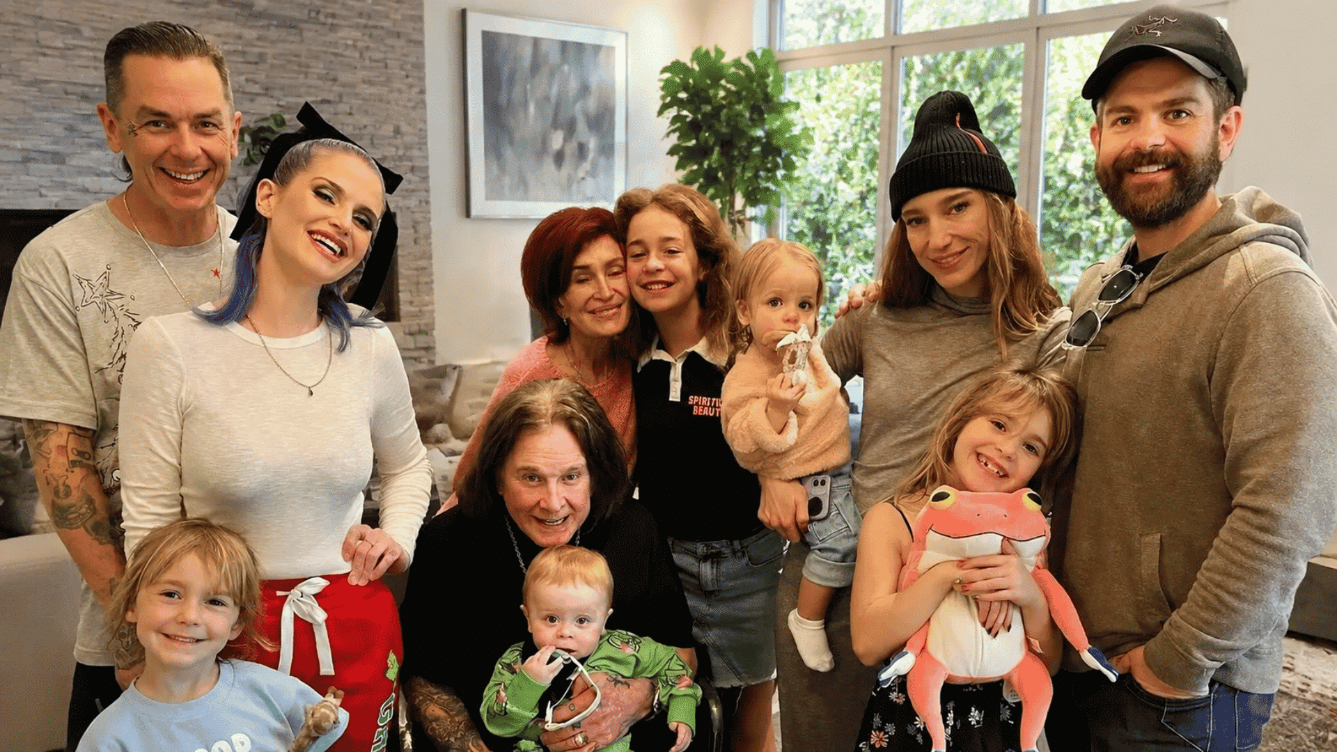A group photo of Sharon Osbourne surrounded by her children and grandchildren smiling together indoors.