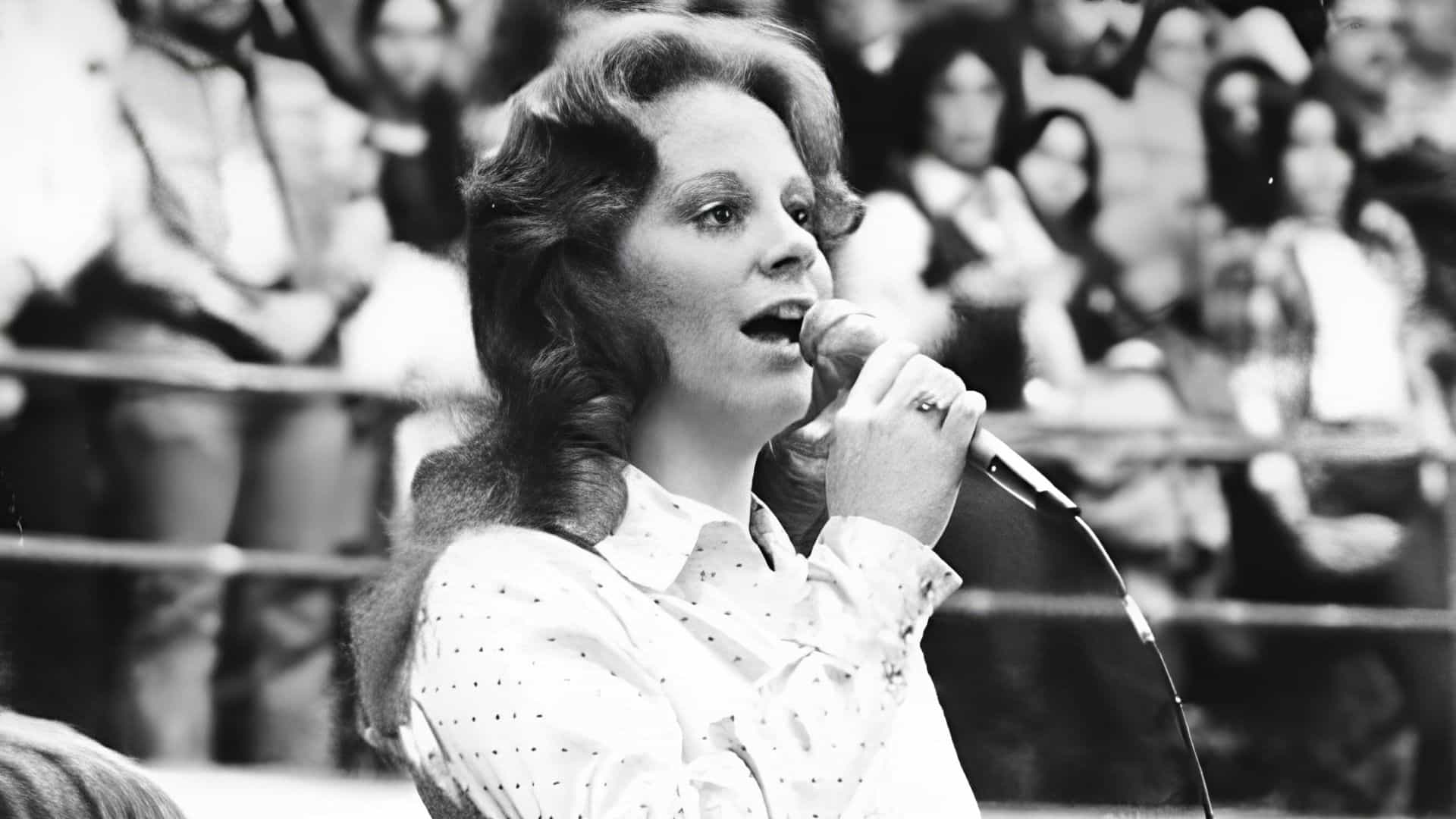 Young Reba McEntire singing on stage into a microphone during an early country music performance