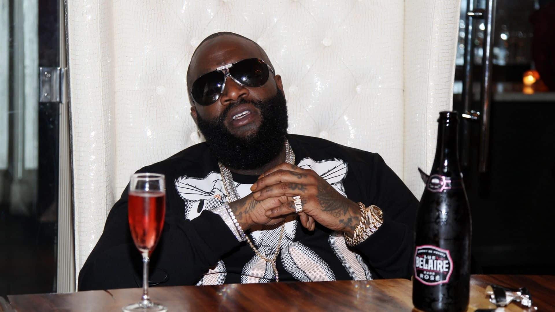Rick Ross seated beside a bottle and glass of Luc Belaire Rosé sparkling wine