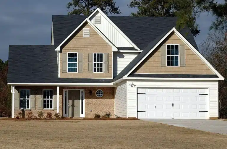 Two-story suburban house with beige siding and dark roof under cloudy sky