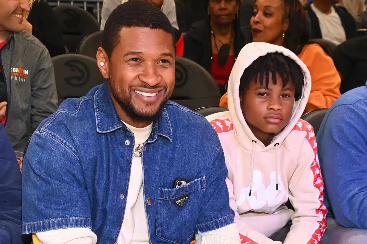  Usher with his eldest son, Cinco, at a basketball game, with spectators seated behind them.