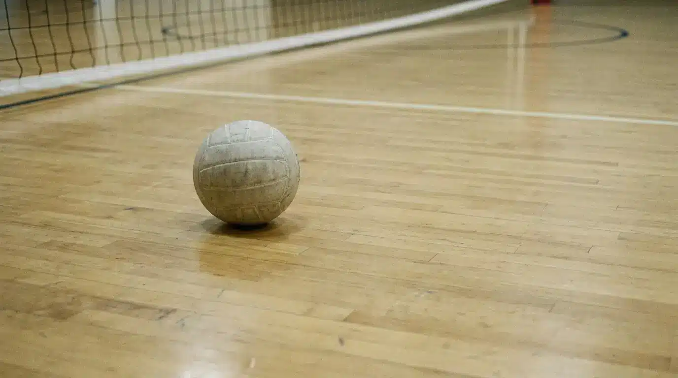 Volleyball on wooden indoor court floor with net in background