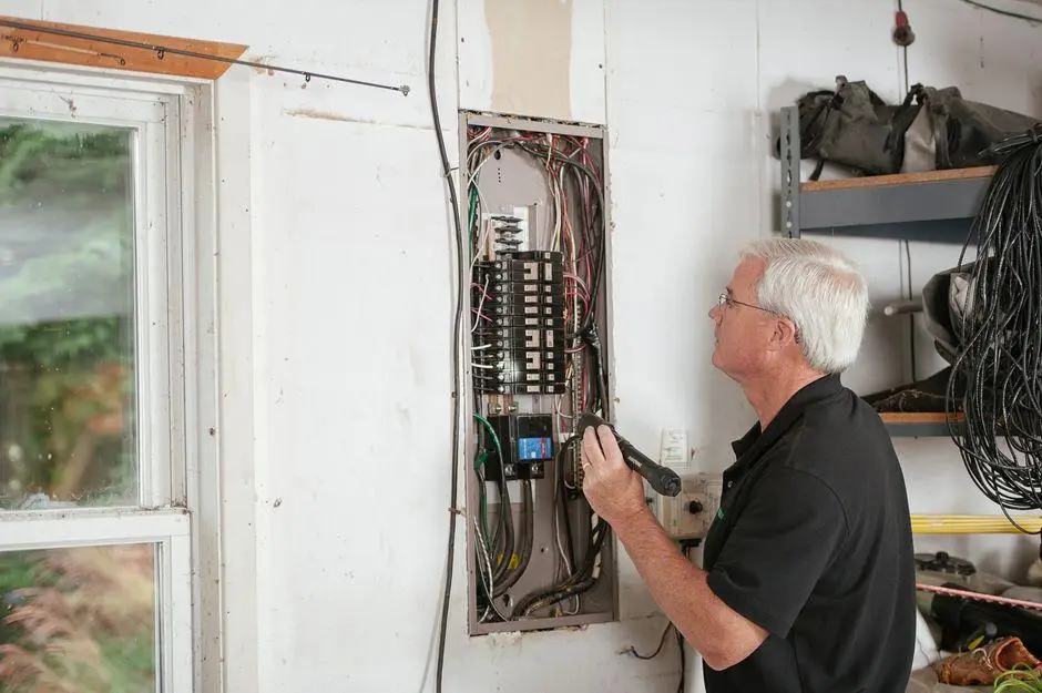 Electrician examining circuit breaker panel in a garage with tools and wiring visible