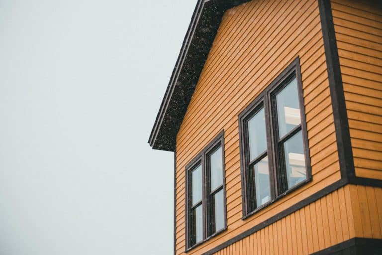 Yellow wooden house exterior with dark trim and large windows under cloudy sky