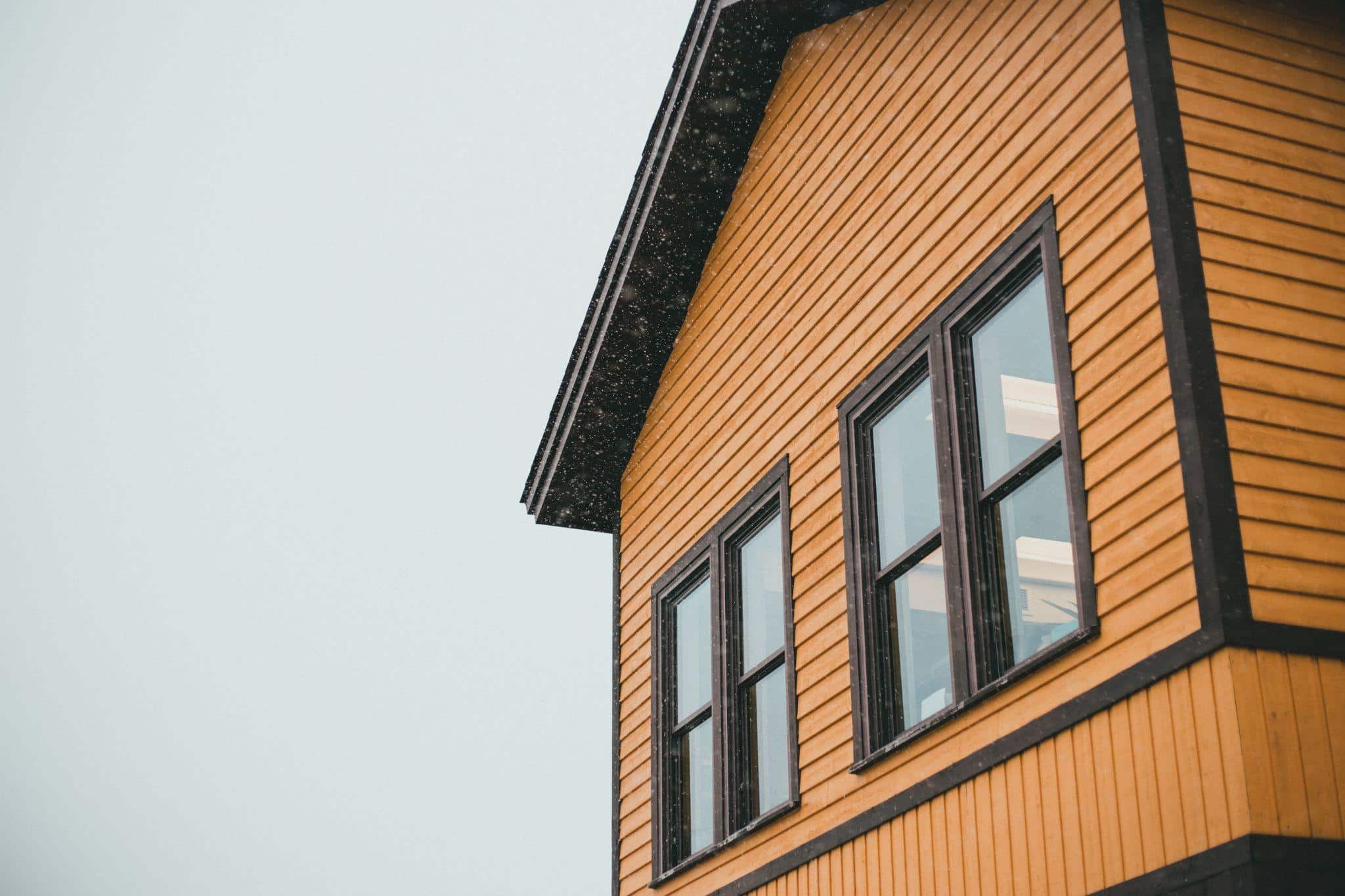 Yellow wooden house exterior with dark trim and large windows under cloudy sky