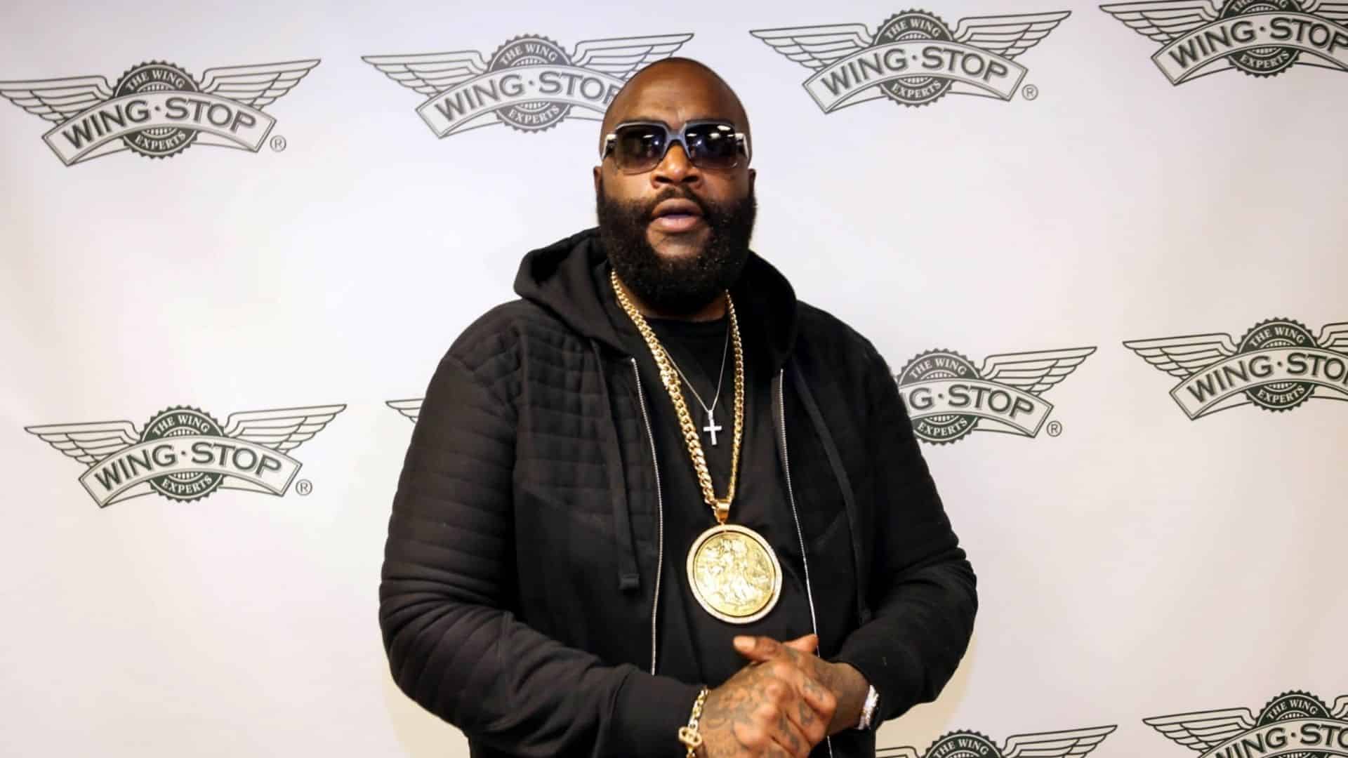 Rick Ross posing in front of a Wingstop logo backdrop