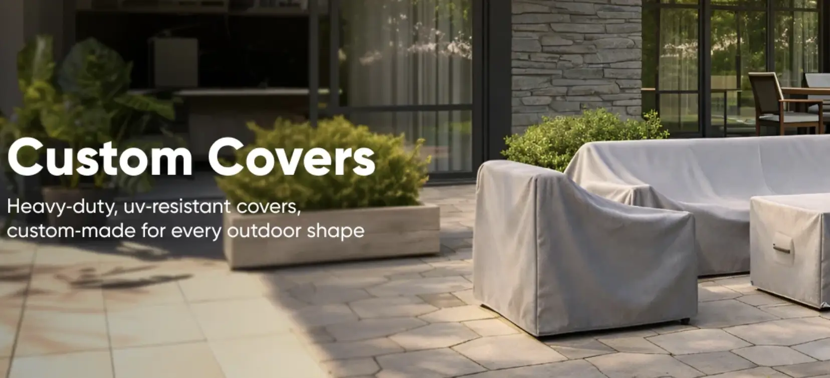 Outdoor patio furniture covered with gray protective covers, surrounded by leafy green plants